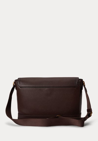 Σκούρο καφέ δερμάτινη τσάντα ταχυδρόμου με ρυθμιζόμενο υφασμάτινο ιμάντα ώμου και εξαρτήματα σε χρυσό τόνο, πάνω σε απλό ανοιχτό φόντο.