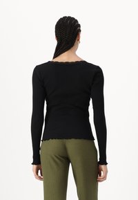 Tricou lung negru cu fante ribbed, având un decolteu și un tiv cu margine ondulată. Asortat cu pantaloni verzi ce au un aspect ribbed, prezentând o siluetă ajustată.