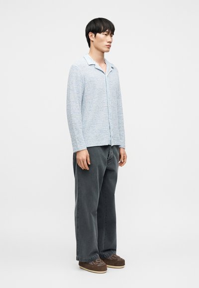 Chemise rayée bleu clair avec col, boutonnée sur le devant, manches longues, associée à un pantalon ample gris foncé et des chaussures marron à enfiler.