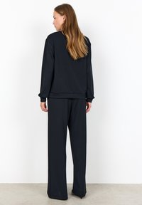 Black athletic set featuring a pullover with dotted texture on sleeves and loose-fitting pants with a smooth fabric finish.