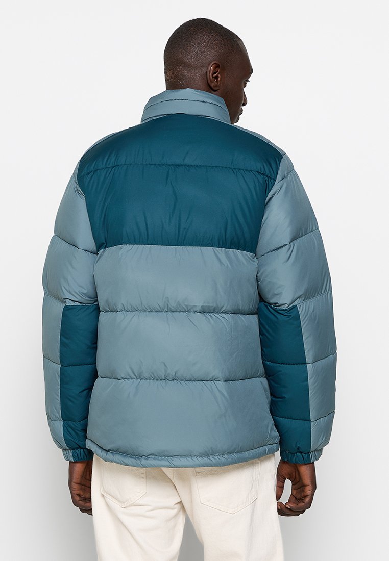 Giacca a vento in diverse tonalità di blu e verde, con un collare alto, design a righe e polsini elastici. Morbido, con texture trapuntata.