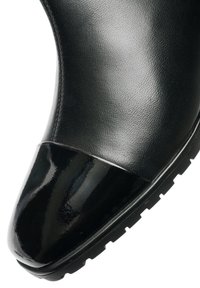 Zwarte enkelboot gemaakt van gestructureerd leer met een glanzende patenten neus. Voorzien van een dikke zwarte rubberen zool en een naadloos ontwerp.