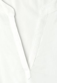 Gros plan sur l'encolure d'une chemise blanche présentant un col en V avec des coutures visibles et un léger pli sur le col.