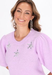 Fliederfarbener Strickpullover mit kurzen, puffartigen Ärmeln, der auf der Vorderseite mit drei dekorativen Strass-Schneeflockenakzenten versehen ist. Weiche Textur.
