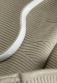 Beige ribbelstof met een gladde witte rand, die een intrigerende structuur en gebogen lijnen toont, wat een gelaagd uiterlijk creëert.