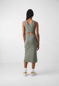 Grön ribbade klänning med V-back design och utskärning i midjan. Modellen har vita strumpor och sneakers med gula accenter.