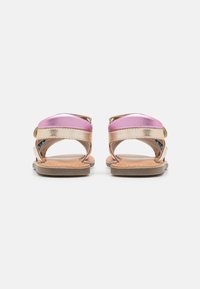 Sandales à bout fermé avec des lanières métalliques roses et dorées, dotées d'une semelle plate couleur sable et de boucles réglables pour un ajustement sécurisé.