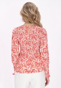 Blusa stampata floreale con tonalità di rosa e pesca, vita arricciata, maniche lunghe con polsini aderenti e dettaglio a chiave sulla schiena.