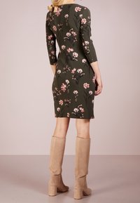 Květinové šaty z tmavozeleného materiálu s 3/4 rukávy. Jsou zdobeny růžovými a bílými květinami, mají těsně přiléhající siluetu a jsou kombinovány s béžovými botami po kolena.