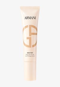Tubo beige chiaro con una finitura lucida e una sfumatura bianco-oro, con la scritta "ARMANI" e un logo circolare. Il testo riporta "SKIN TINT long-wear & care."
