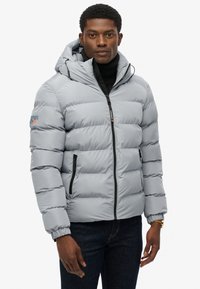 Giacca imbottita di colore grigio chiaro con cappuccio, dotata di zip frontale, polsini elasticizzati e tasche laterali, realizzata in materiale liscio e resistente all'acqua.
