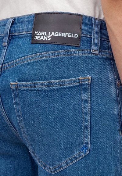 Vue arrière d'un jean en denim bleu avec une étiquette noire portant la mention Karl Lagerfeld Jeans au-dessus de la poche arrière.