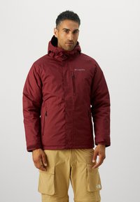Maroon insulated jacket with a hood, front zip, and two side pockets. Features a logo on the chest and elastic cuffs. Worn over khaki cargo pants.