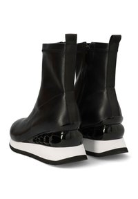 Botas Ángeles sintéticas negras con una textura suave, paneles laterales elásticos y un distintivo tacón de cuña brillante en negro y blanco.