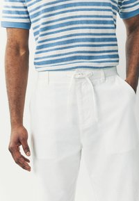 Valged linaülikonnad, millel on sõlmitav vöökoht, kombineeritud sinise ja valge triibulise kootud särgiga, millel on lühikesed varrukad ja reljeefne muster.