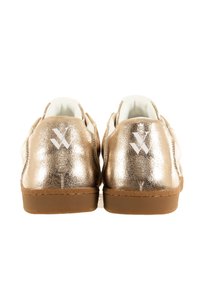 Gouden metallic sneakers met witte accenten, met een gladde textuur en rubberen zolen, van achteraf weergegeven. Witte logo op elke hak.