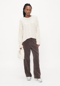 Debeli kremasti džemper s pletenicom, smešani široki kargo pantaloni od kordura i mala bela torbica. Patike sivo-srebrnih akcenata.