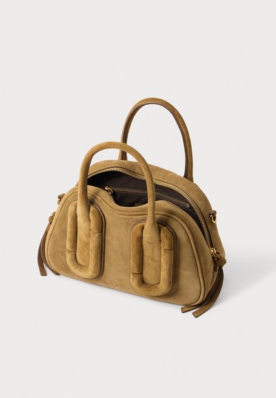 Sac à main en daim brun clair avec deux poignées arrondies, une fermeture éclair dorée partiellement ouverte et des boucles décoratives matelassées sur le devant.
