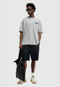 T-shirt cinza oversized com mangas curtas, detalhe do logo preto; combinado com calções pretos, bolsa preta e sapatilhas bege.