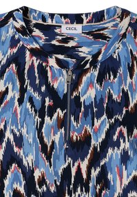 Gros plan sur un chemisier à motifs abstraits bleus, blancs, marron et rose avec encolure ronde et fermeture éclair argentée à l'avant, étiqueté « Cecil ».