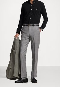 Svart långärmad skjorta med knappar, grå skräddarsydd byxor, svarta läderskor och en grå houndstooth-blazer över armen.