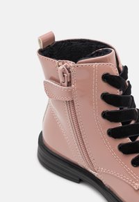 Botte en cuir verni rose avec un intérieur texturé noir, des lacets à l'avant et une fermeture éclair sur le côté avec une languette en tissu. Semelle en caoutchouc noir.