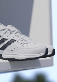 Paire de chaussures de sport blanches avec des rayures noires reposant sur un rebord blanc devant un arrière-plan extérieur flou.