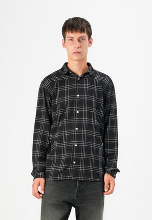 Black and white plaid shirt with a button-up design, featuring a soft texture and long sleeves. Model wearing dark jeans.