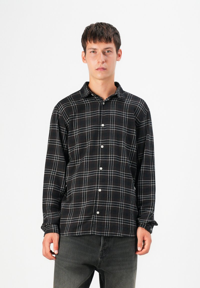 Svart och vit rutig skjorta med knapplåsdesign, i en mjuk textur och långa ärmar. Modellen bär mörka jeans.