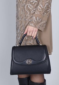 Borsa a struttura nera con finitura testurizzata, caratterizzata da un logo monogramma dorato sul fronte, manico superiore e chiusura sicura.