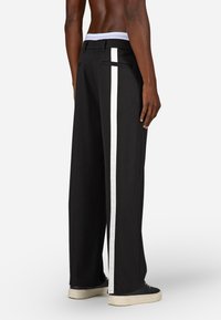 Platas melnas bikses ar baltu sānu svītru, gludu tekst�ūru un plakanu jostasvietu ar kontrastējošu iekšējo oderi.