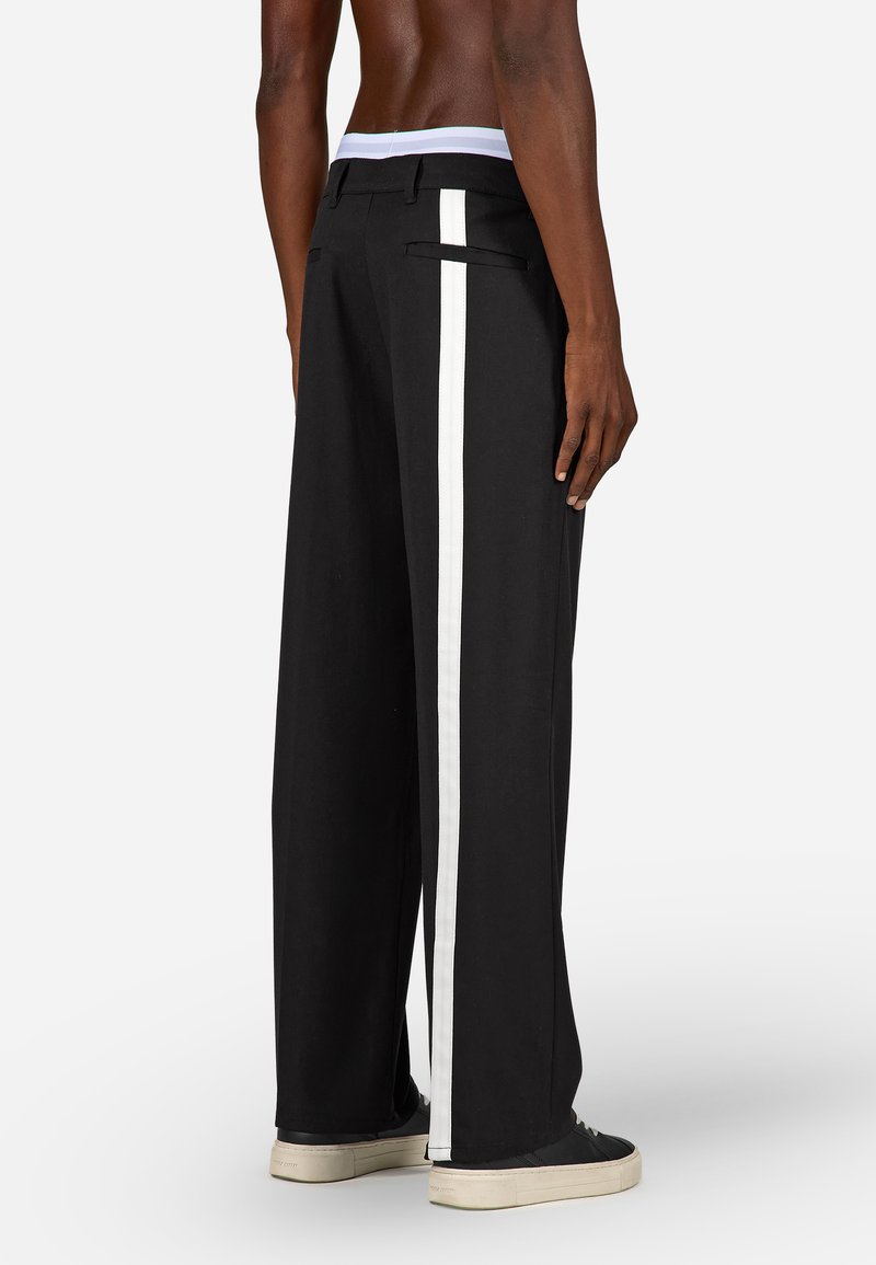 Platas melnas bikses ar baltu sānu svītru, gludu tekstūru un plakanu jostasvietu ar kontrastējošu iekšējo oderi.