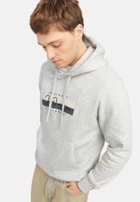 Sudadera gris con un bolsillo frontal, con un gráfico de logo oscuro y cordones. Textura suave, puños y bajo acanalados. Ajuste casual.