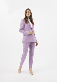 Fialový oblek na míru se sakem na jedno knoflík, úzkými kalhotami a bílou blůzou. Hladká tkanina a minimalistický design.