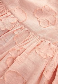 Rosa Stoff mit floraler Stickerei, der mit Rüscheln und einem weichen, strukturierten Aussehen verziert ist. Die Blumen haben ausgefranste Kanten, die zusätzliche Details verleihen.