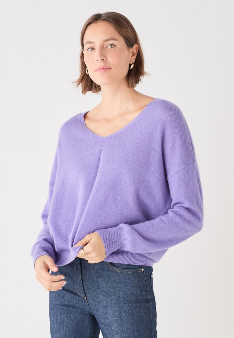 Lila V-halsad tröja i mjukt stickat material med sänkta axlar och ribbade ärmmuddar, ihop med mörkblå denimjeans.