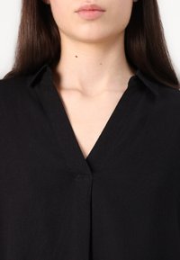 Black shirt with a v-neck design, button detail at the collar, and a textured fabric. The fabric appears lightweight and slightly wrinkled.