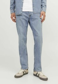 Svijetloplave traperice, ravnog kroja, s izblijeđenim završetkom. Uparene s bijelom majicom i srebrnim tenisicama s crnim akcentima i bijelim vezicama.