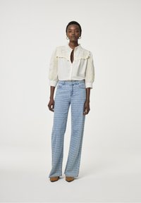 Witte button-up blouse met kantdetail op de schouders, gecombineerd met blauwe, gebloemde flared jeans en bruine puntige schoenen.