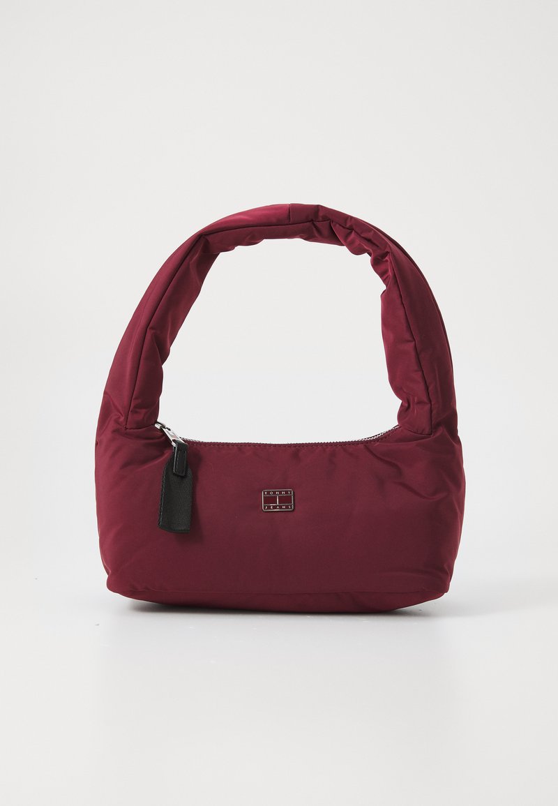 Geantă din material textil burgundy, căptușită, cu un mâner curbat și adunat, închidere cu fermoar și un mic tag din piele neagră. Logo-ul este vizibil pe partea din față.