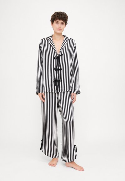 Black and white striped pajama set with a button-up shirt featuring a collar and decorative ties. Loose-fitting pants with side slits.
