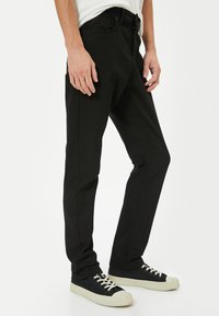 Pantalones de mezclilla negra con un ajuste slim, que presentan un diseño clásico de cinco bolsillos. La tela es suave, con detalles de costura sutiles a lo largo de las costuras.