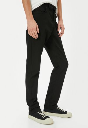 Pantalon en denim noir avec une coupe slim, doté d'un design classique à cinq poches. Le tissu est lisse, avec des détails de couture subtils le long des coutures.