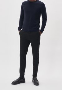 Granatowy sweter z okrągłym dekoltem i długimi rękawami. Czarne spodnie o wąskim kroju. Czarne mokasyny z teksturowanym wykończeniem. Proste, jednolite kolory w całym zestawie.