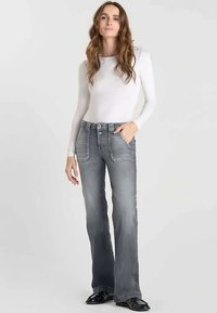 Jean en denim gris évasé avec une texture douce, doté de poches avant, d'une fermeture à double bouton et de détails de couture contrastants.