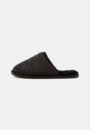 Zapatilla negra de tipo slip-on con parte superior acolchada y forro interior de suave piel, mostrada de perfil sobre un fondo blanco.
