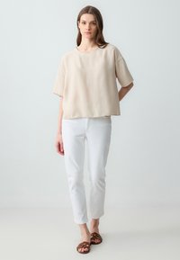 Beige, kort mouwen top met een ronde hals; gecombineerd met witte slim-fit jeans en bruine gevlochten sandalen. Eenvoudig, ontspannen ontwerp.
