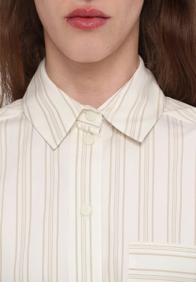 Kreemi värvi kraepluus, millel on vertikaalsed beežid triibud, nuppude ja rinnataskuga. Sile kangas klassikalise disainiga.