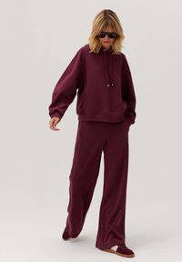 Burgundowa hoodie z kieszenią, luźny krój i szerokie rękawy, w połączeniu z pasującymi spodniami o szerokich nogawkach. Miękka tkanina i minimalne detale w designie.