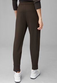 Braune, enganliegende Jogginghosen mit schmal zulaufenden Beinen und umgeschlagenen Knöcheln. Aus weichem Stoff gefertigt, mit hohem Bund. Kombiniert mit weißen Sneakers.